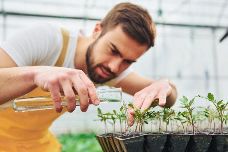 Young greenhouse worker in yellow uniform have job inside of hothouse.